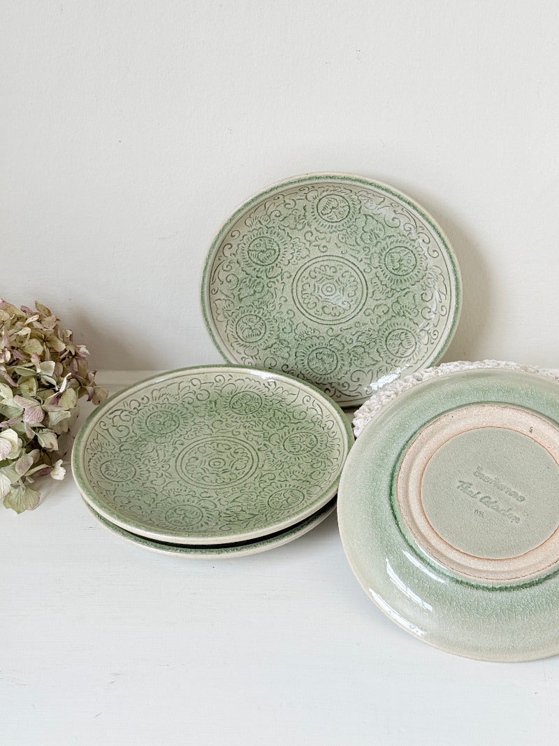 Set of four Thai stoneware plates with soft green celadon glaze on white surface