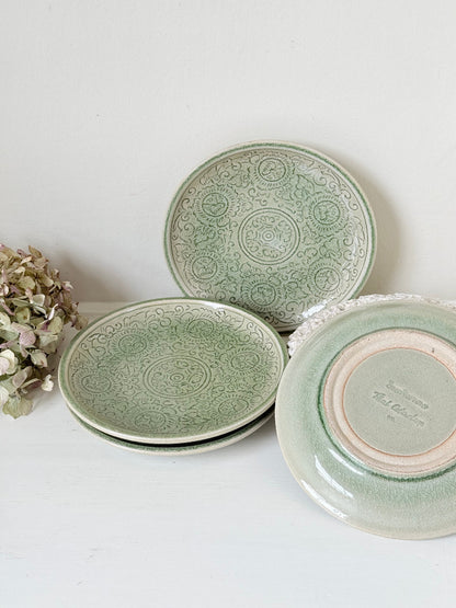 Set of four Thai stoneware plates with soft green celadon glaze on white surface