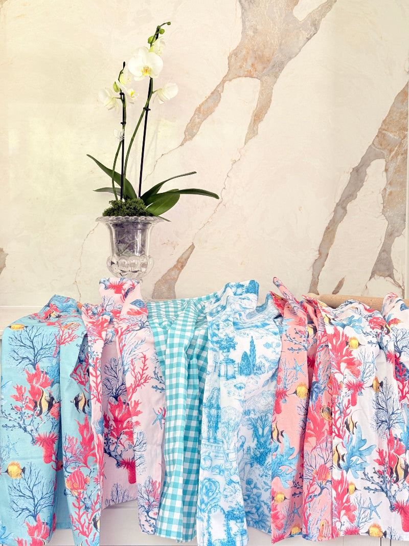 Warm peach coral and tropical fish print cotton tea towel with wooden forks on a marble surface beside cut glass