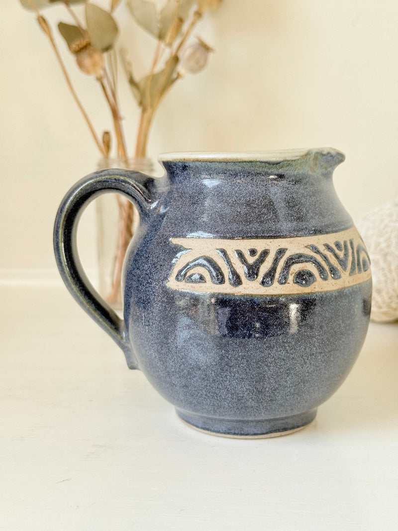Studio pottery milk jug with deep blue glaze and cream geometric band, photographed on a white surface