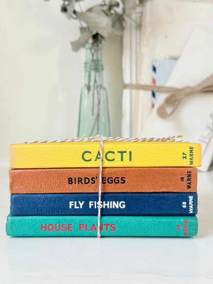 A stack of four textured fabric-covered books tied with twine, featuring the titles &