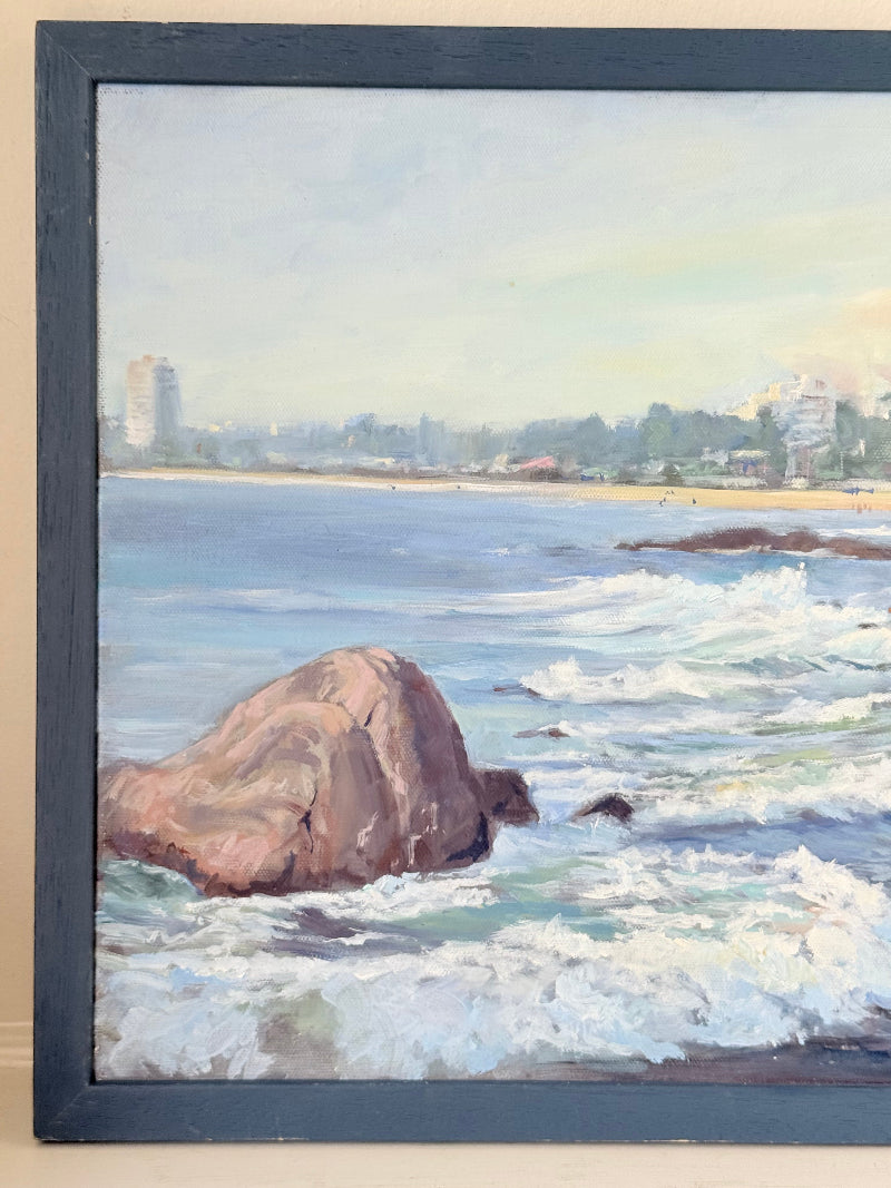 Original oil painting of waves crashing against rocks, signed seascape in slate blue wooden frame on white surface

