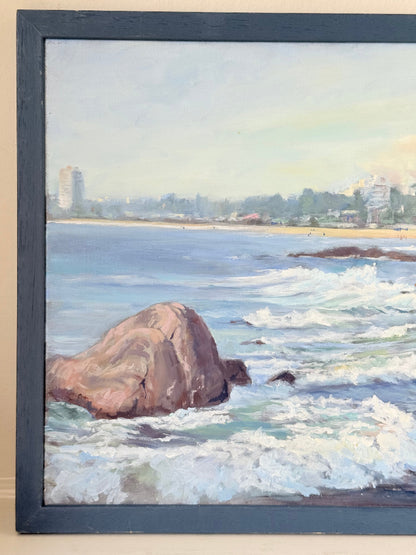 Original oil painting of waves crashing against rocks, signed seascape in slate blue wooden frame on white surface

