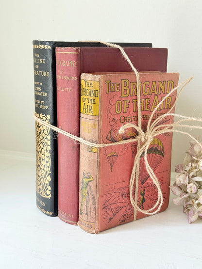 Vintage decorative book bundle in red and black with gilt detailing tied with twine, photographed on a white surface