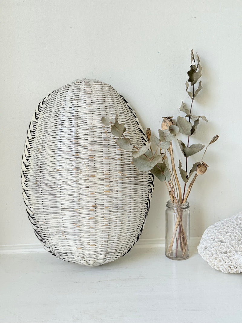 Vintage white chippy wicker basket with oval shape and worn painted finish, photographed on white surface.