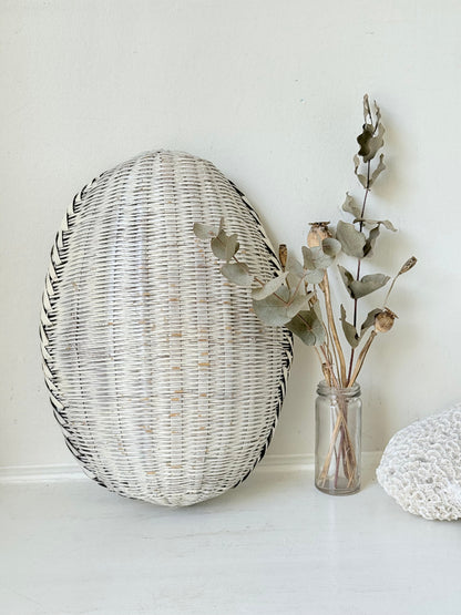 Vintage white chippy wicker basket with oval shape and worn painted finish, photographed on white surface.