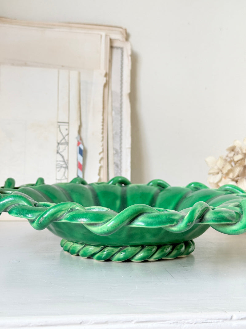 A glossy green ceramic bowl with a twisted rope-style rim and base, displayed on a light surface against a soft neutral background.