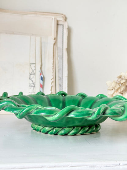 A glossy green ceramic bowl with a twisted rope-style rim and base, displayed on a light surface against a soft neutral background.