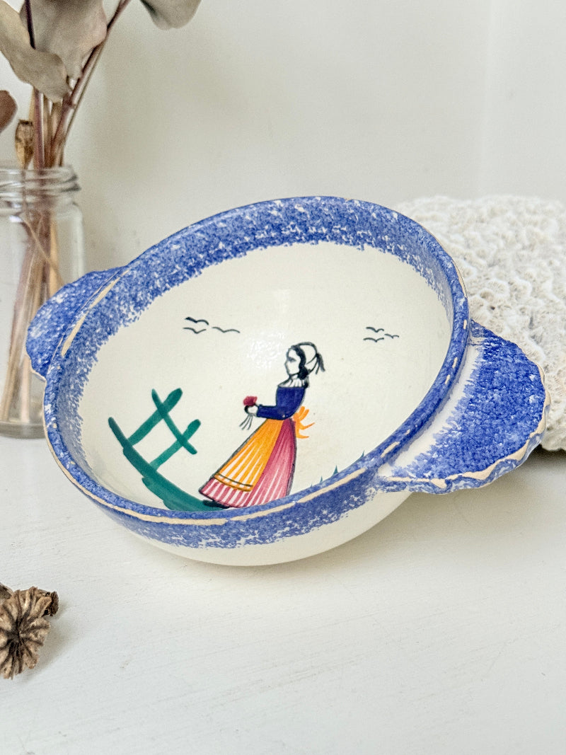Quimper faience olive bowl with Petit Breton figure and blue speckled rim photographed on a white surface