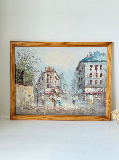 Vintage oil painting of European street scene with buildings and awnings in wooden frame photographed on a white surface

