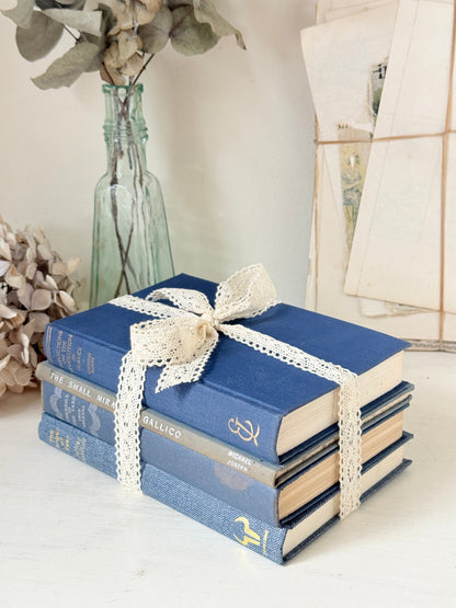 Bundle of vintage blue cloth books with gilt spines tied with ivory lace ribbon for shelf and table styling
