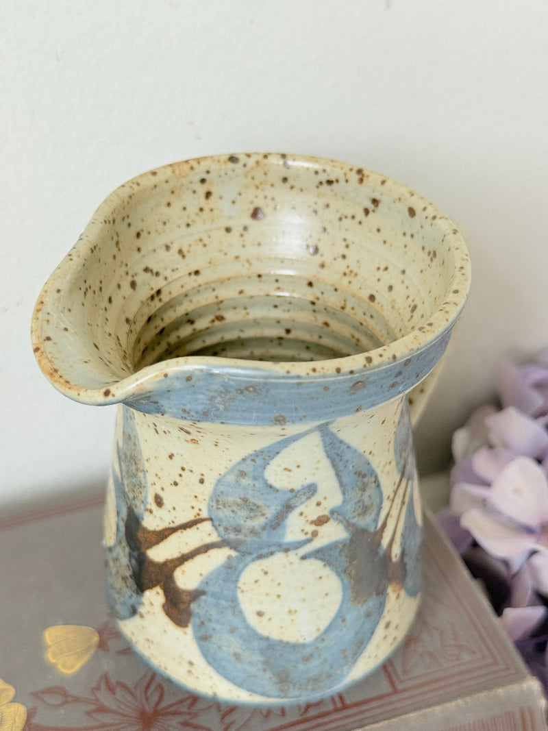 Vintage studio pottery jug with blue floral decoration on speckled cream glaze, photographed on white surface