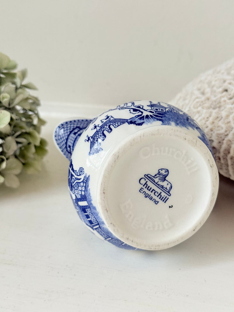 Vintage Churchill Blue Willow milk jug in blue and white ceramic photographed on a white surface.