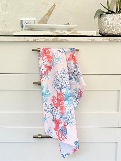 Pale pink coral and seaweed print cotton tea towel with wooden spoon on a marble surface