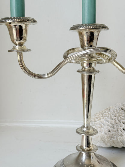 Vintage silver plated three arm candelabra with gadrooned detail and blue green taper candles styled on a white surface