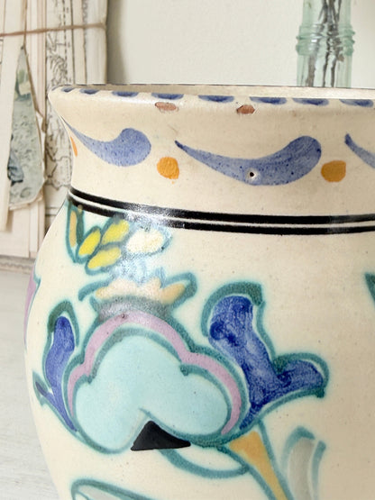 Hand painted floral pottery vase in blue and green on cream, photographed on a white surface