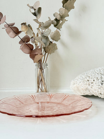 Vintage blush pink pressed glass plate with floral pattern photographed on a white surface