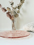 Vintage blush pink pressed glass plate with floral pattern photographed on a white surface