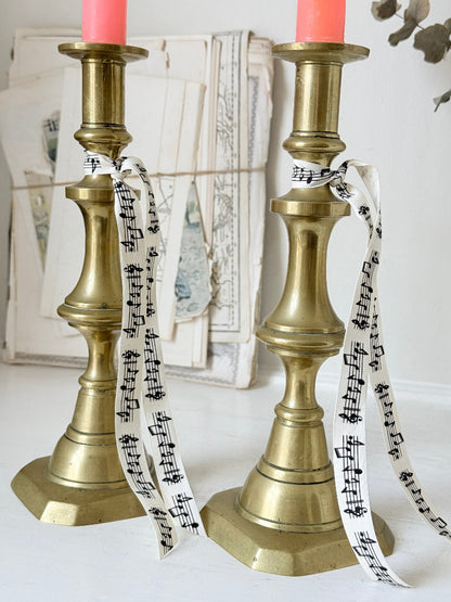 Pair of antique brass candlesticks with turned baluster stems and stepped bases holding coral tapers