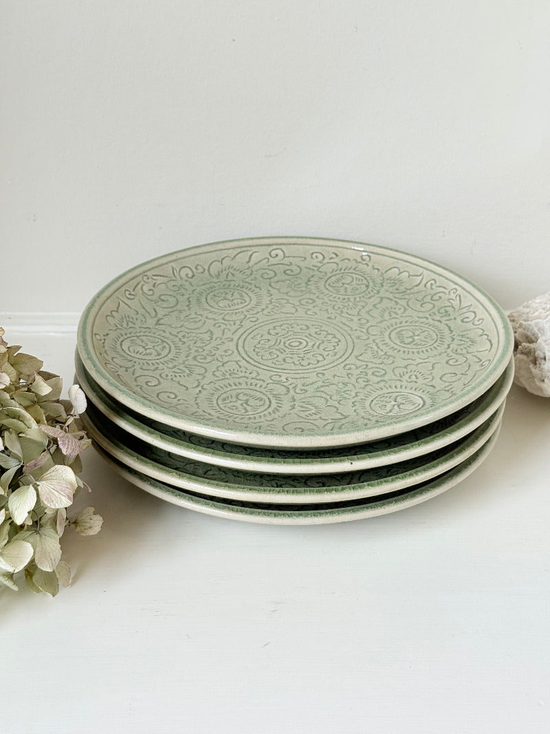 Set of four large Thai celadon stoneware plates in soft green glaze with raised pattern, photographed on a white surface
