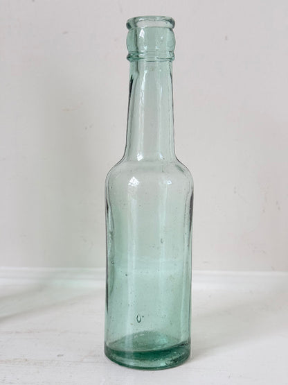 Trio of antique aqua and green glass bottles with embossed lettering, photographed on a white surface