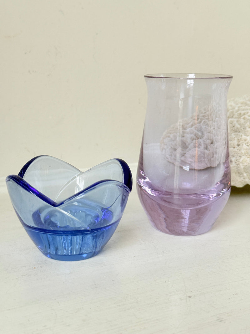 Blue Bormioli Rocco glass candlestick and lilac glass vase photographed on a white surface