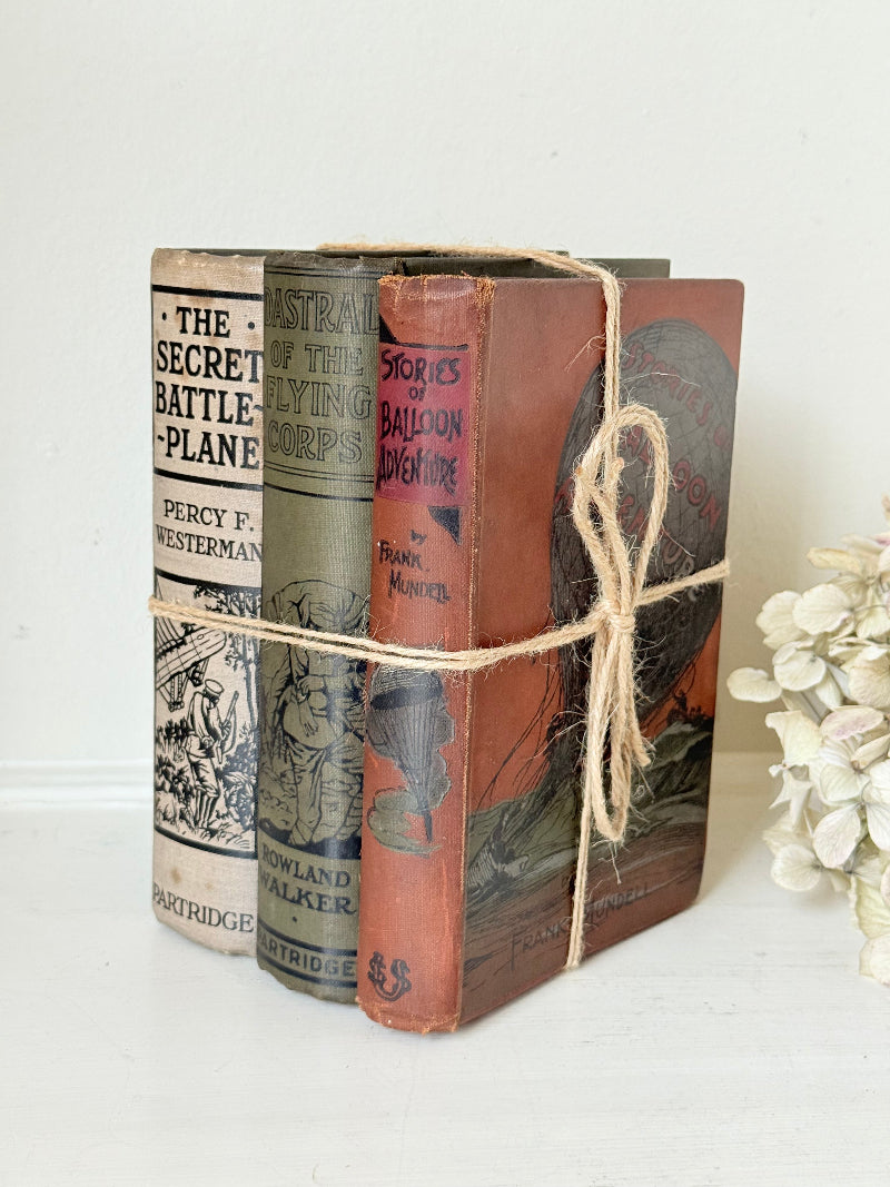 Vintage decorative book bundle in red, olive green and cream tied with twine, photographed on a white surface