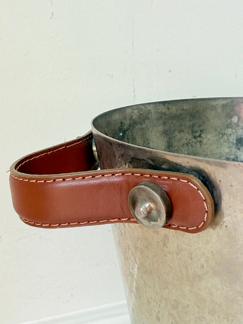 Vintage metal wine cooler with leather handles and tapered form, photographed on white surface.