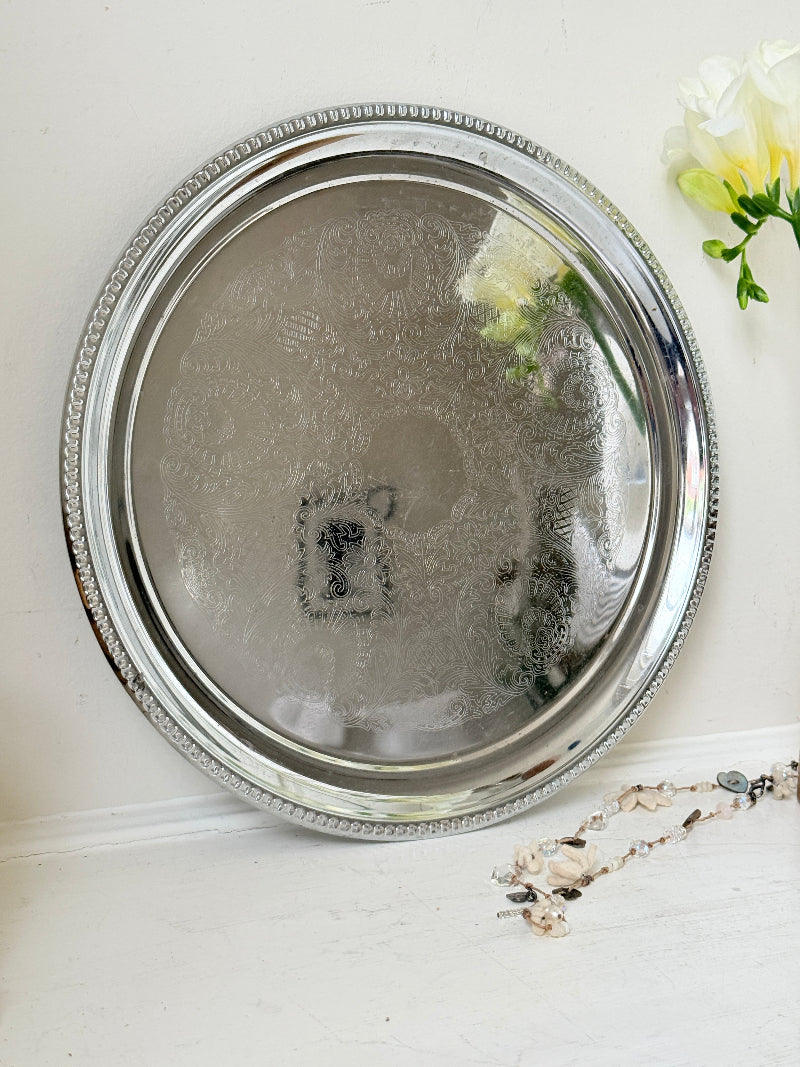 Vintage silver tone round tray with beaded edge, engraved surface detail and reflective finish for drinks or vanity styling