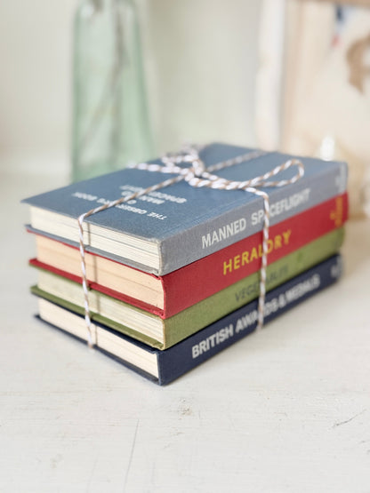 A stack of four miniature hardcover books tied together with white string, featuring titles including &