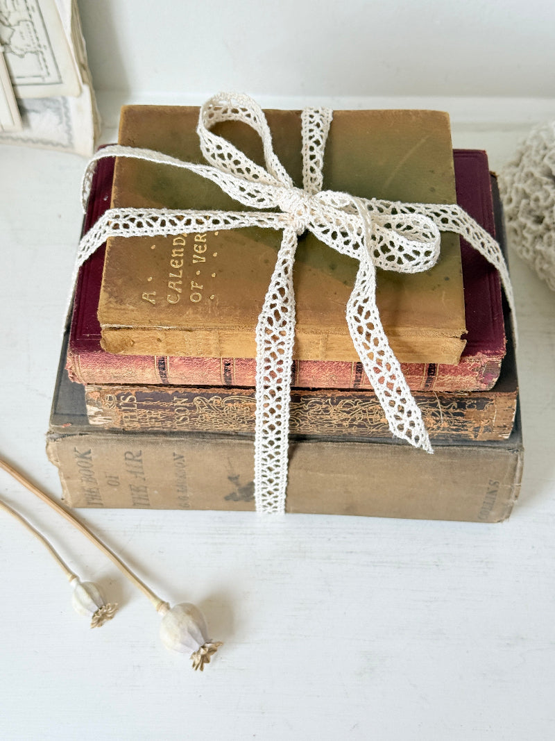 Antique decorative book bundle with faded hardback covers, aged pages and neutral lace tie for vintage interior styling