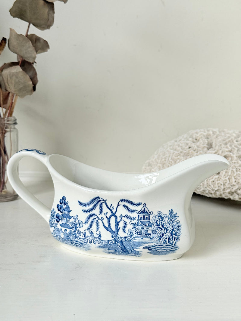 Vintage blue and white ceramic sauce boat with willow pattern photographed on a white surface