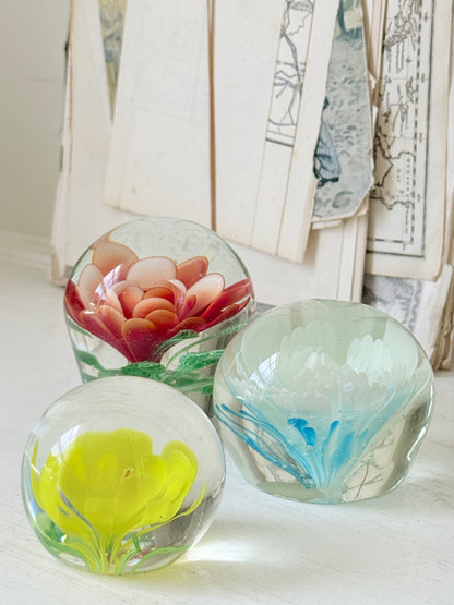 Trio of vintage glass paperweights with red flower, yellow flower and turquoise swirl decoration in clear coloured glass