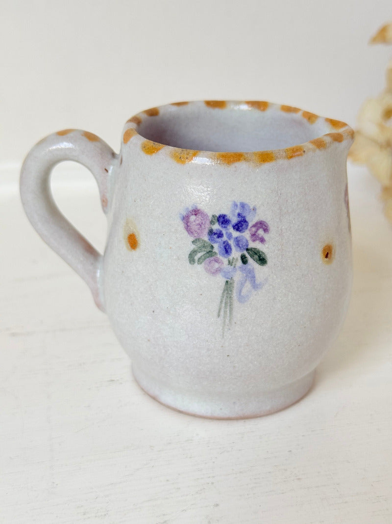 vintage studio pottery milk jug with hand painted lilac flowers and ochre rim photographed on white surface