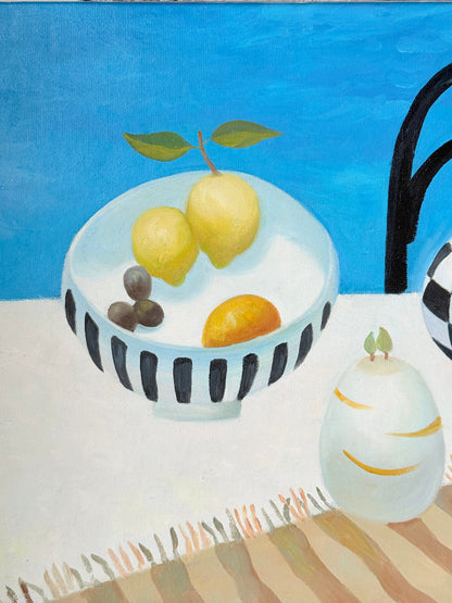 Still life oil painting showing fruit bowl and striped jug on a blue background, framed in white wood, photographed on a white surface.