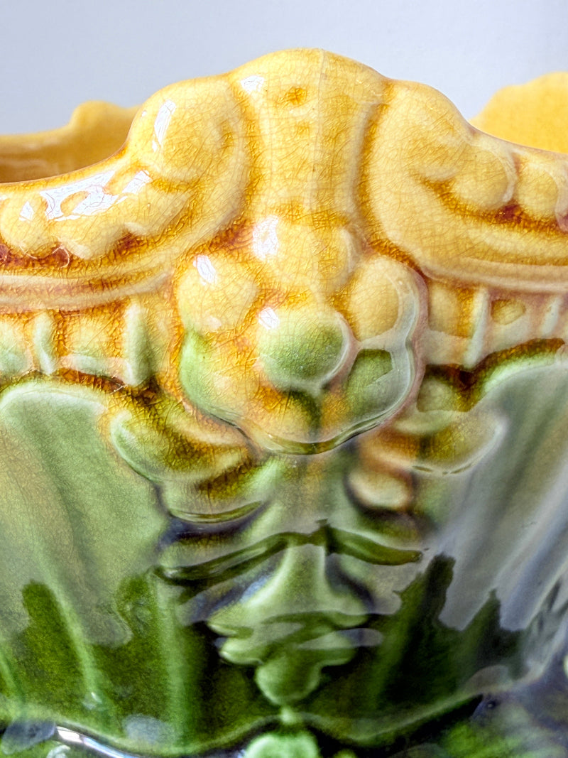 Close-up of a decorative ceramic planter with a sculpted floral relief and glossy glaze in yellow, green, and brown tones.