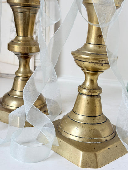 Pair of tall antique brass candlesticks with knopped columns and octagonal stepped bases holding blue and green tapers
