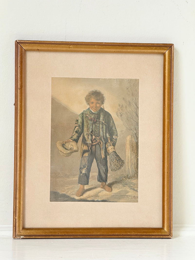 Vintage print of Little Beggar Boy in muted colours, framed under glass in simple wooden frame, on white surface.