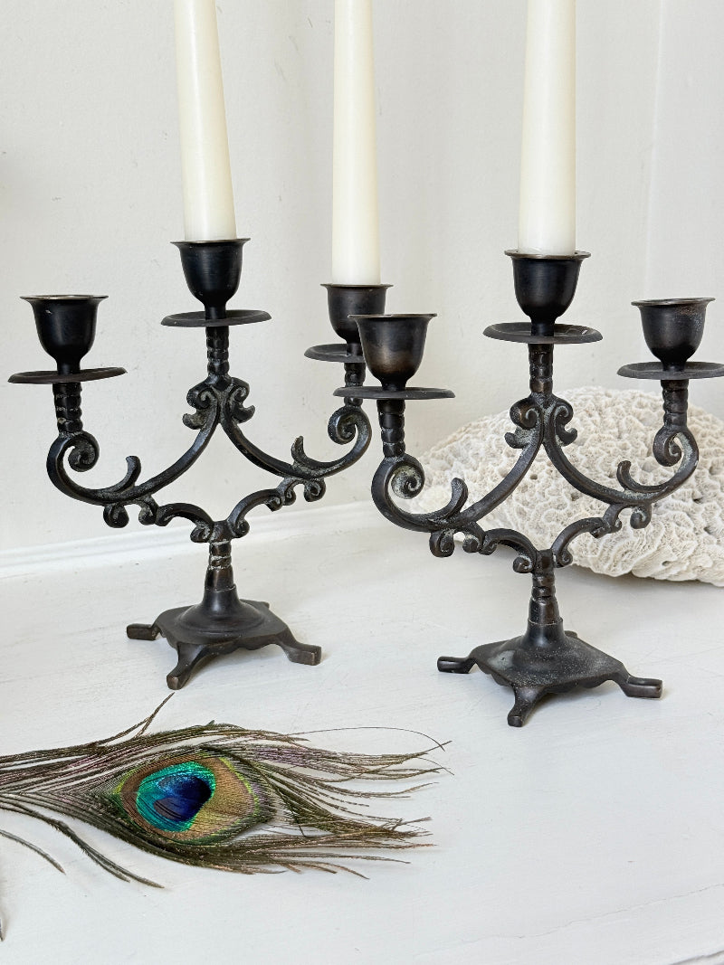 Pair of vintage brass three arm candelabra with scrolling arms and aged patina, photographed on a white surface