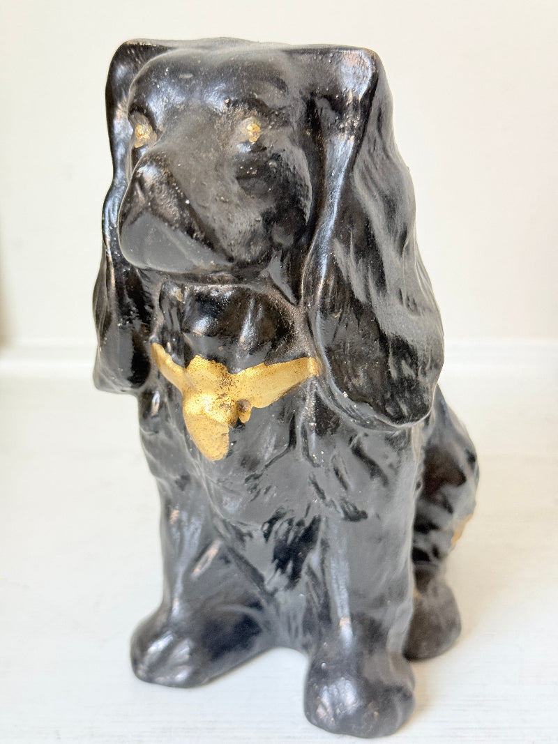 A glossy black ceramic dog figurine with gold painted accents on its chest and ears, standing on a white surface against a white background.