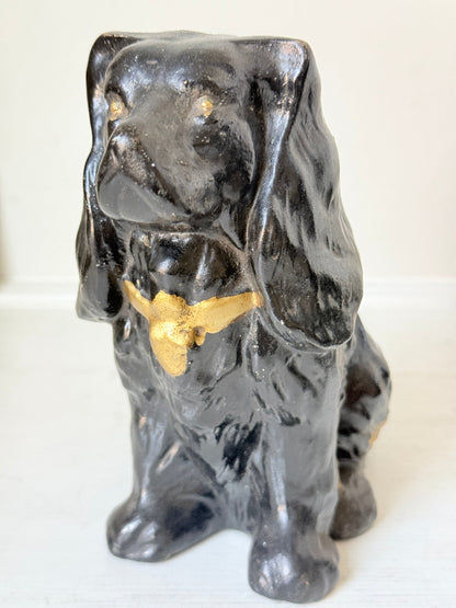 A glossy black ceramic dog figurine with gold painted accents on its chest and ears, standing on a white surface against a white background.