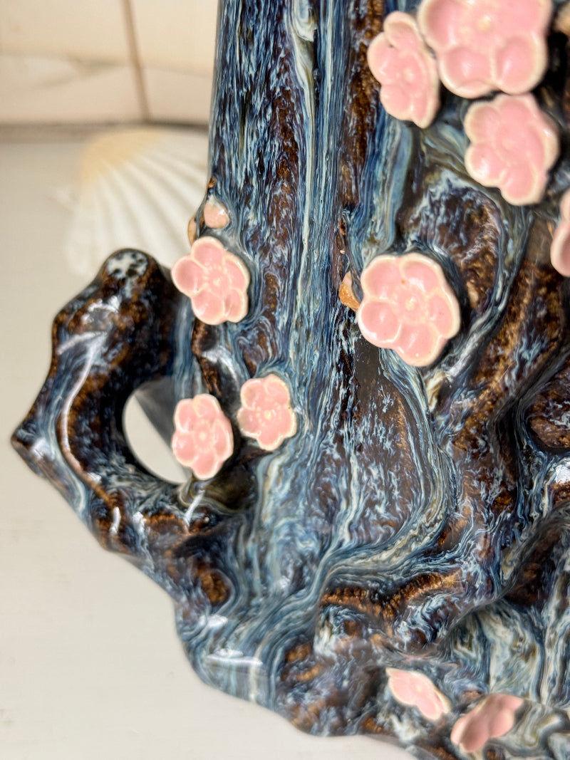 Large ceramic tree trunk vase with applied pink cherry blossom detail, textured bark form and dark drip glaze