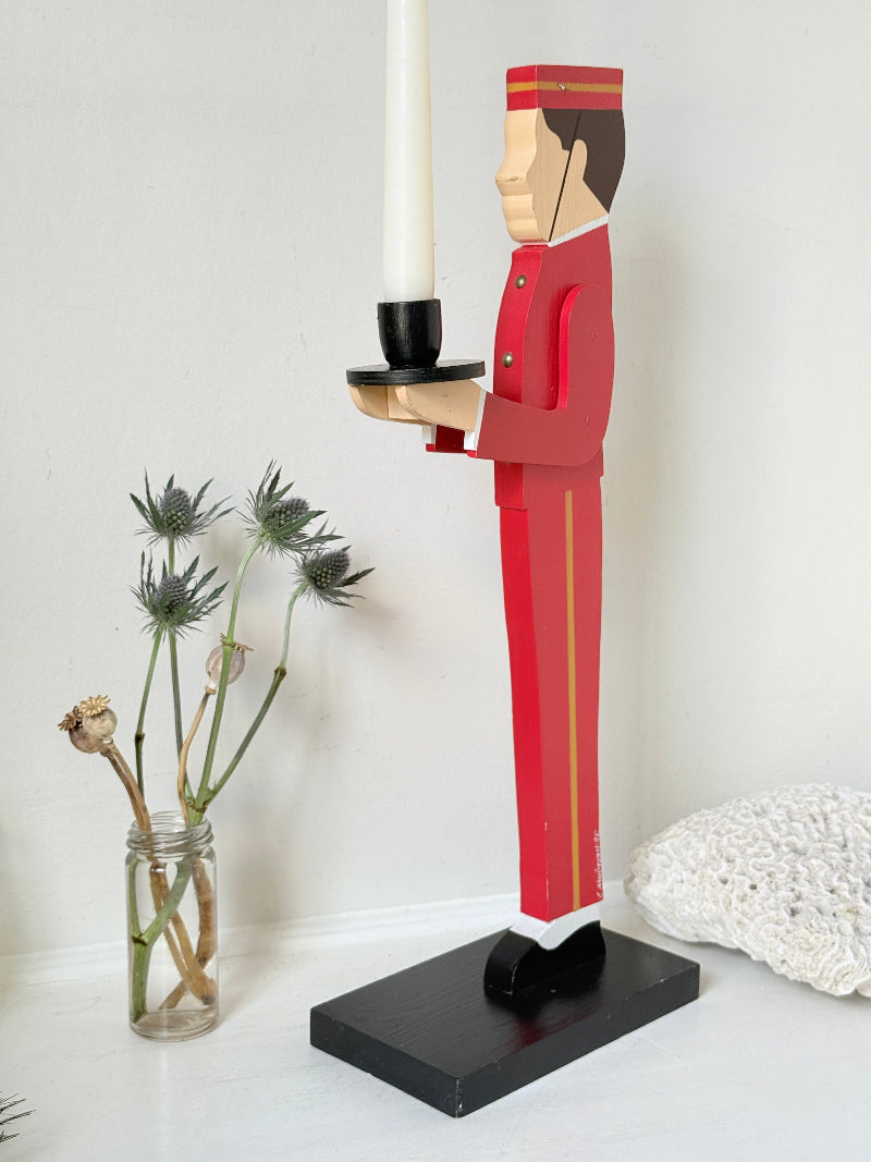 Vintage bellboy candlestick holder in red and black holding a tray with candle, photographed on a white surface