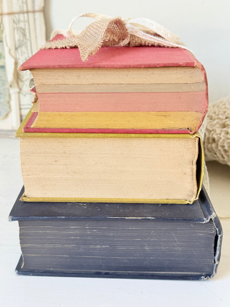 Vintage decorative book bundle in blue yellow and red with aged hardback covers tied with natural ribbon for bookshelf styling