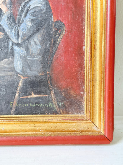 Close-up of a framed painting showing part of a seated figure in blue-gray clothing against a red background, with a distressed gold and red frame.