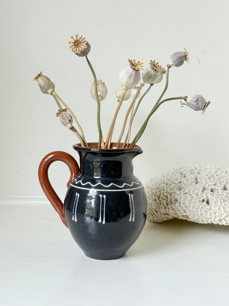 Slipware studio pottery jug with blue glaze and terracotta handle, photographed on a white surface