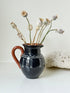 Slipware studio pottery jug with blue glaze and terracotta handle, photographed on a white surface