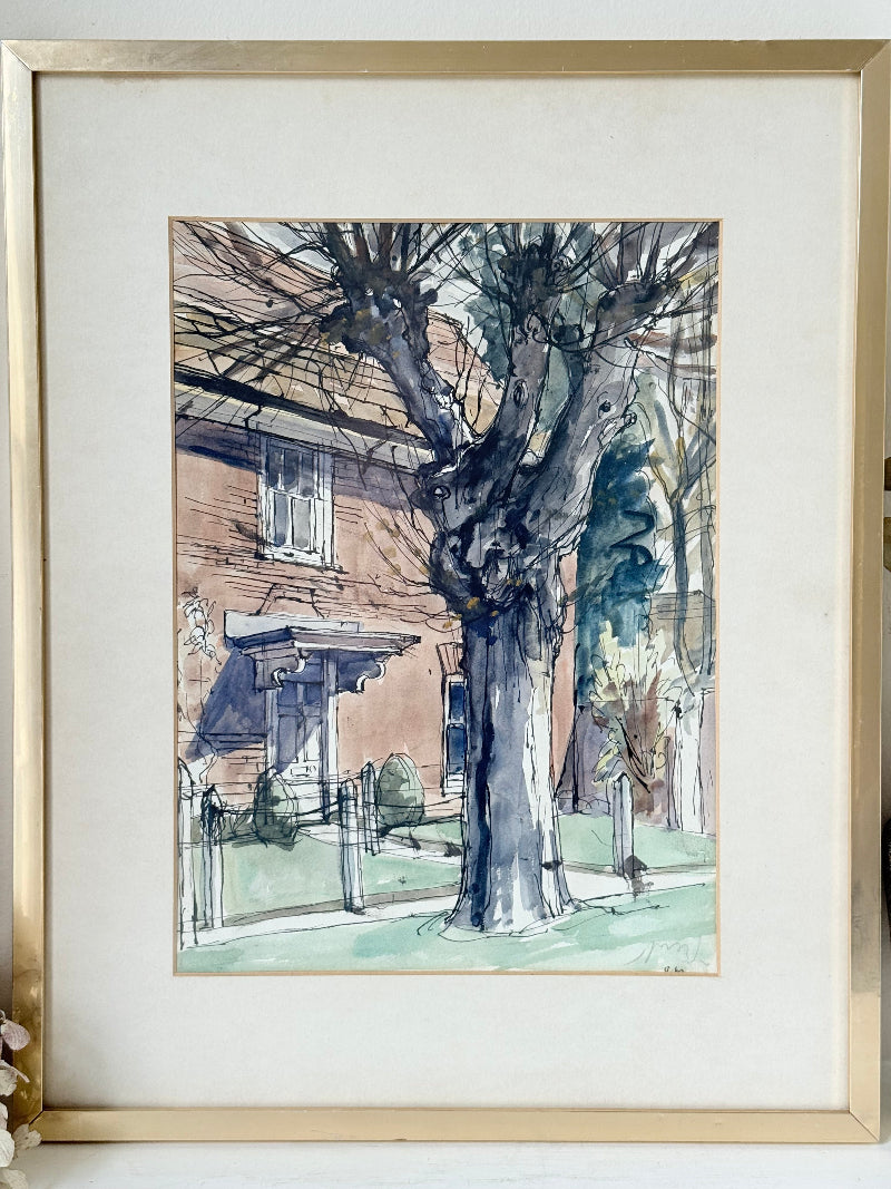 Framed vintage watercolour painting of a large tree and brick house, photographed on a white surface.