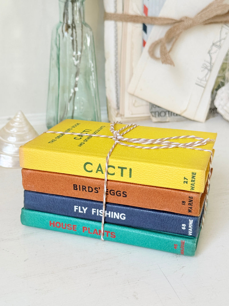 A stack of five hardcover book-shaped coasters tied with twine, featuring colorful spines labeled with titles like &