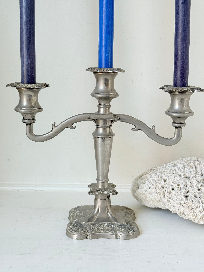 Vintage silver coloured three-arm candelabra with ornate base and soft patina, photographed on a white surface